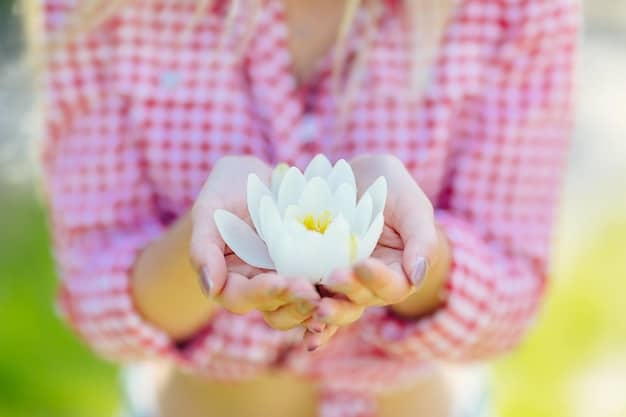 A close-up shot of a person's hands gently holding a lotus flower during a mindfulness meditation session. The background is blurred, emphasizing the person's focus and serenity.