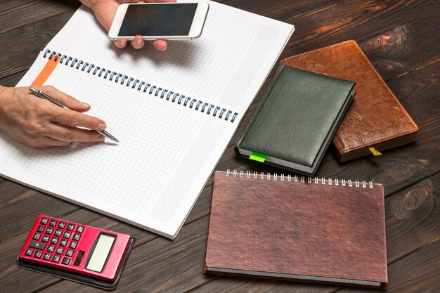 A close-up of a person's hand writing notes with a pen, surrounded by organized tax documents and a calculator. The scene emphasizes focus and efficient information processing.